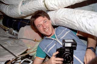 Astronaut Michael Foale (still wearing his Russian flight suit and holding a camera) is photographed in the Mir space station Base Block module. 